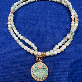 Médaille 26 juin strassée à la main à Paris avec le mot Amour en lettre d'or et un cœur émaillé bombé rose montée sur une chaine perle de verre 74 cm. Le collier peut se porter en sautoir ou en double  ras de cou. La médaille existe également sur chaine de 55cm. Le tout recouvert d'or 24 carats 3 microns. Dessinée, produite, dorée, émaillée et strassée à la main à Paris.